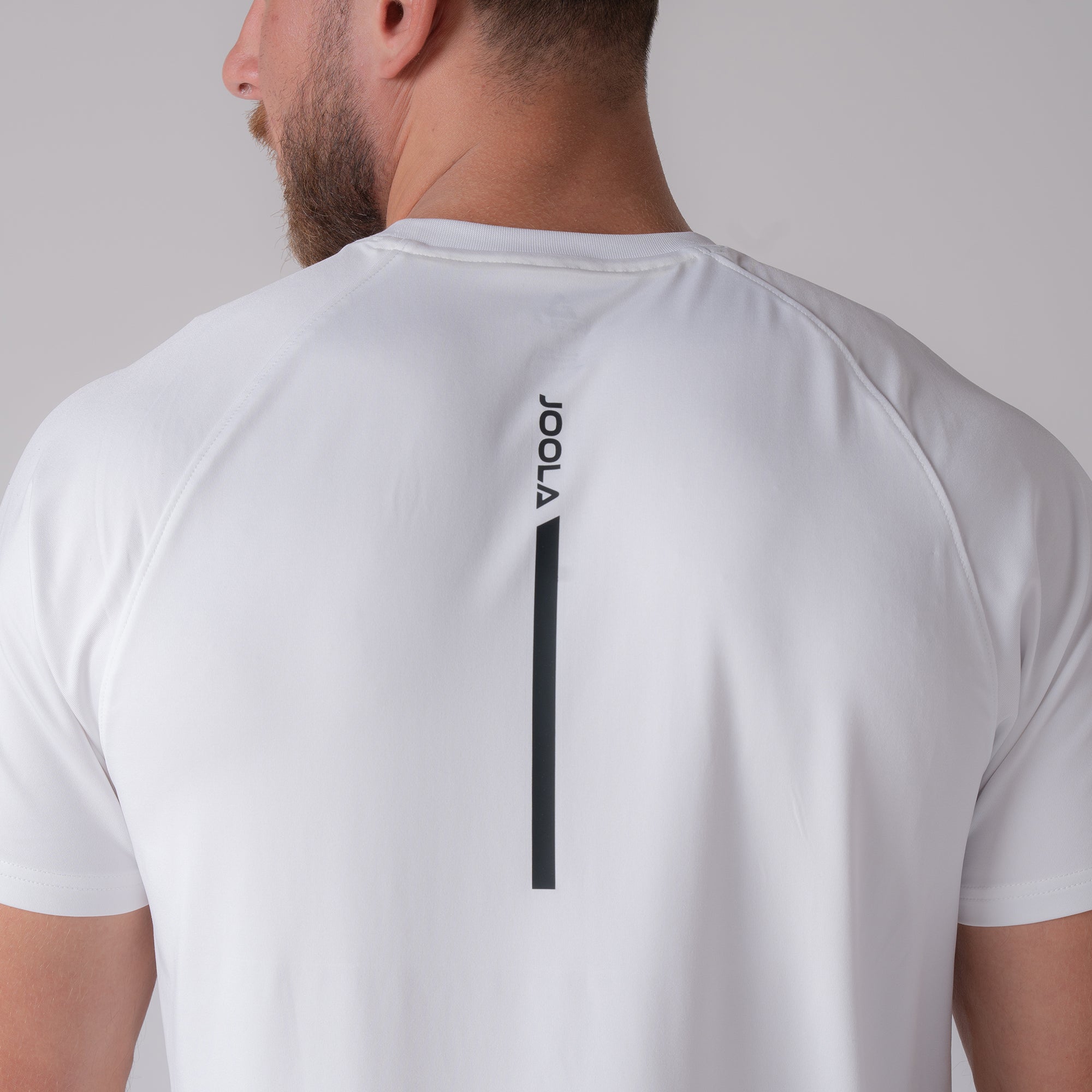 Close up image of the back of a male model who is wearing a JOOLA men's court short sleeve shirt, white with black JOOLA logo down the center.