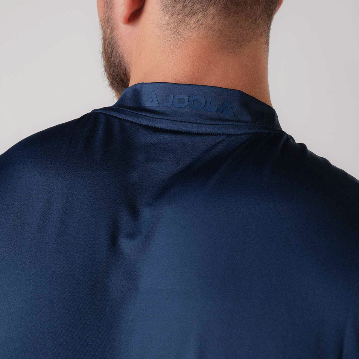 Close up image of the JOOLA logo on the collar of a JOOLA men's court polo, navy.