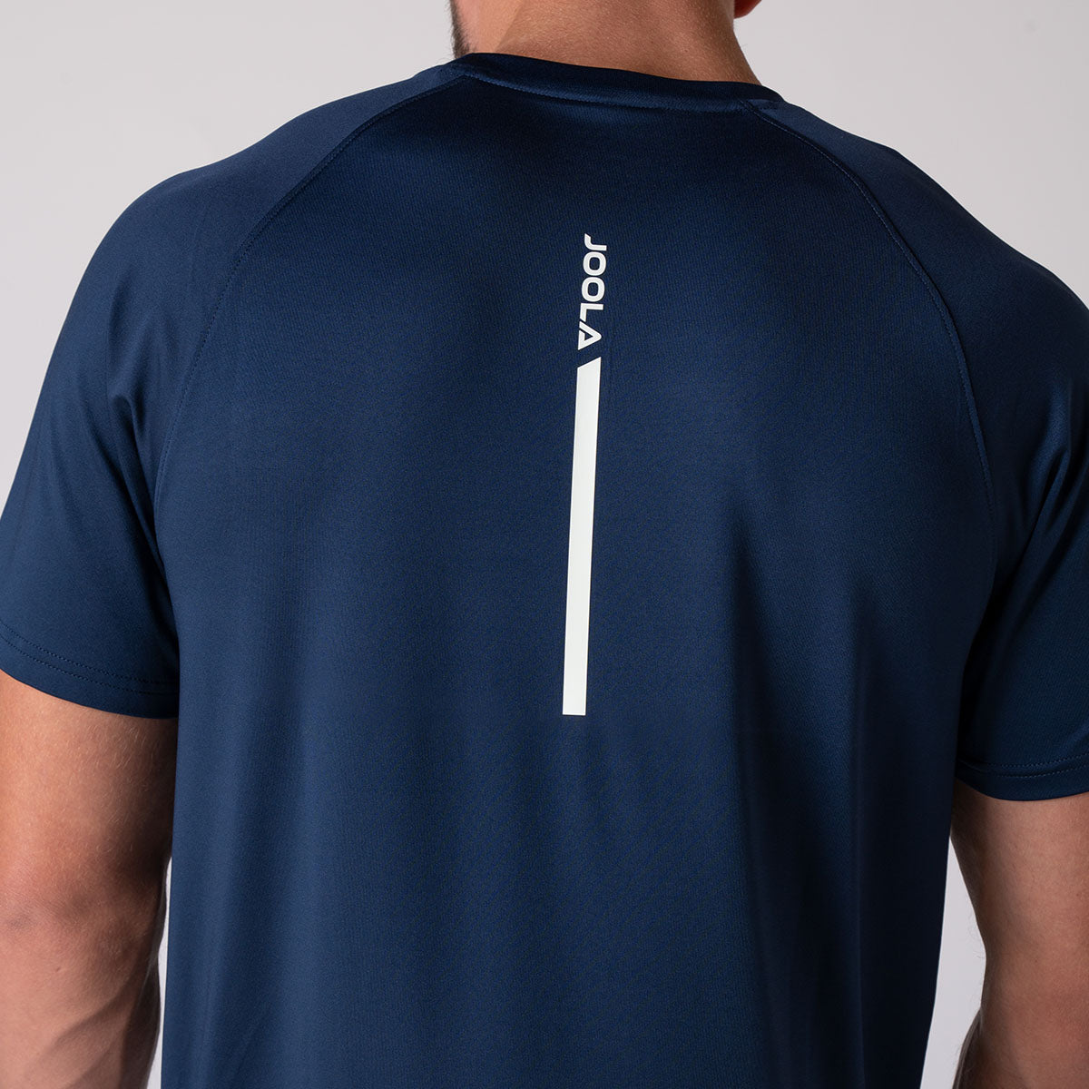 Close up image of the back of a male model who is wearing the JOOLA Men's Court Short Sleeve shirt, navy with white JOOLA logo down the center.
