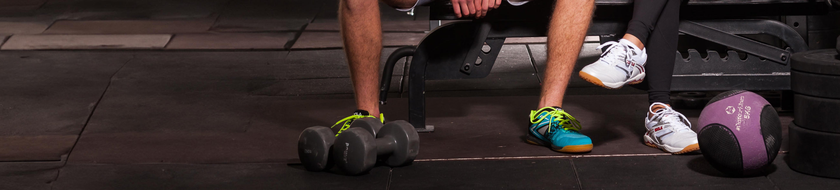 Horizontal banner image of two people, male and female wearing JOOLA shoes at the Gym.