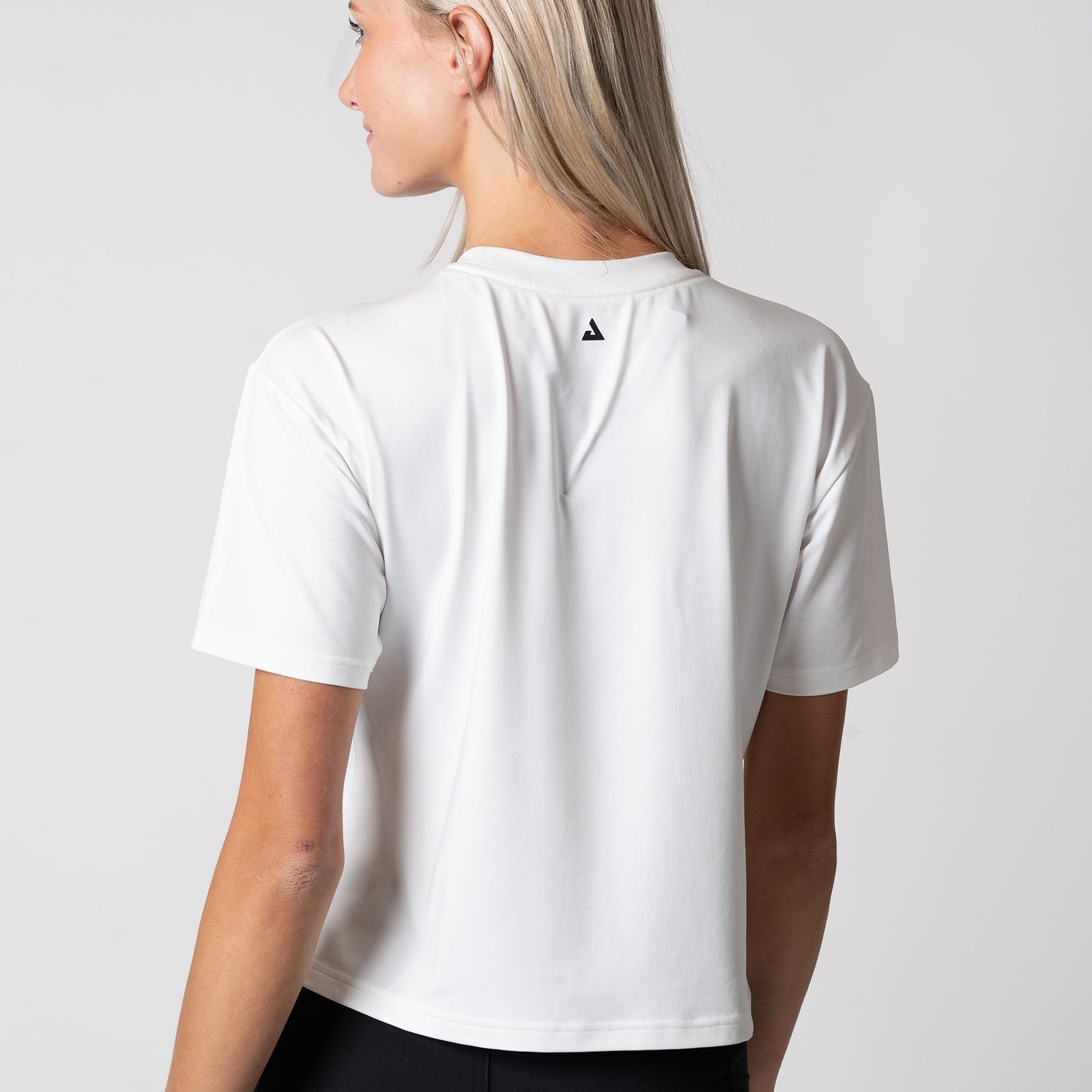 Image showing the back of a female model who is wearing a JOOLA women's court crop tee, white.