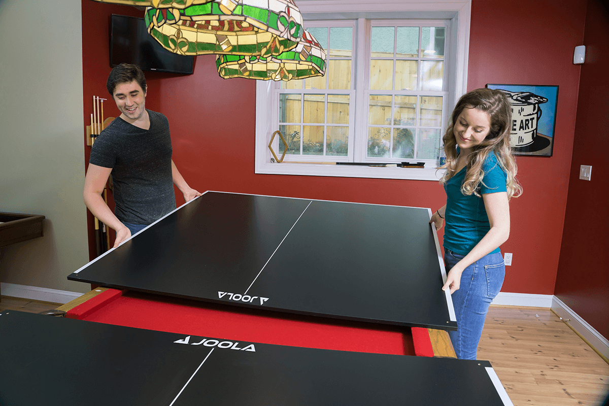 Image of two people putting on the JOOLA Billiard Table Tennis Conversion Top over a billiard table.