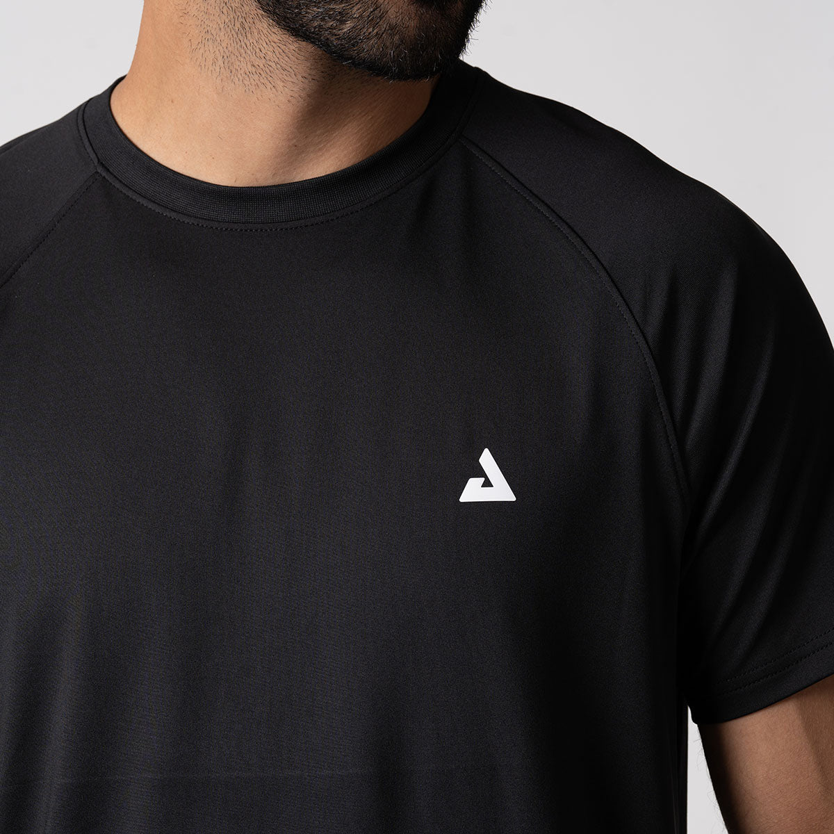 Close up image highlighting the JOOLA trinity logo over the left chest on a JOOLA men's court short sleeve shirt, black.