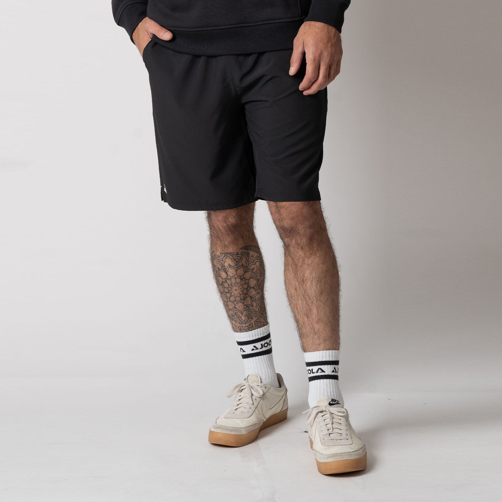 Male model wearing a pair of JOOLA Men's Woven Shorts with a Nine-Inch inseam, black.